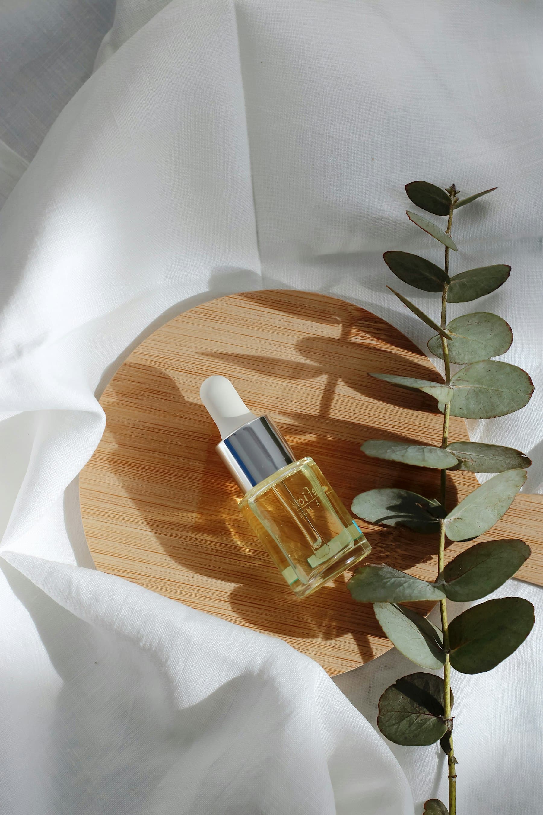 A dropper bottle with a sprig of eucalyptus on soft linen